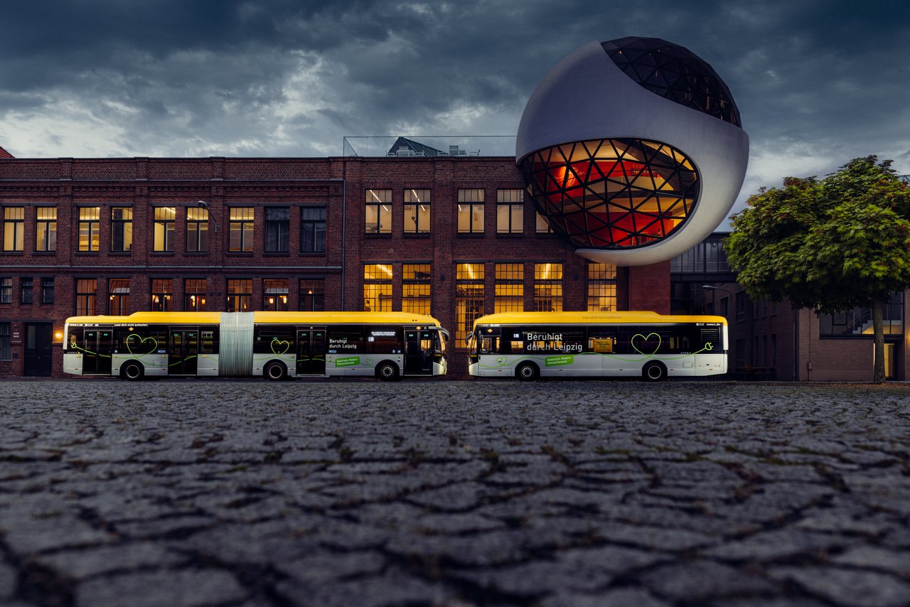 Zwei E-Busse stehen sich gegenüber vor einem Gebäude in der Abenddämmerung