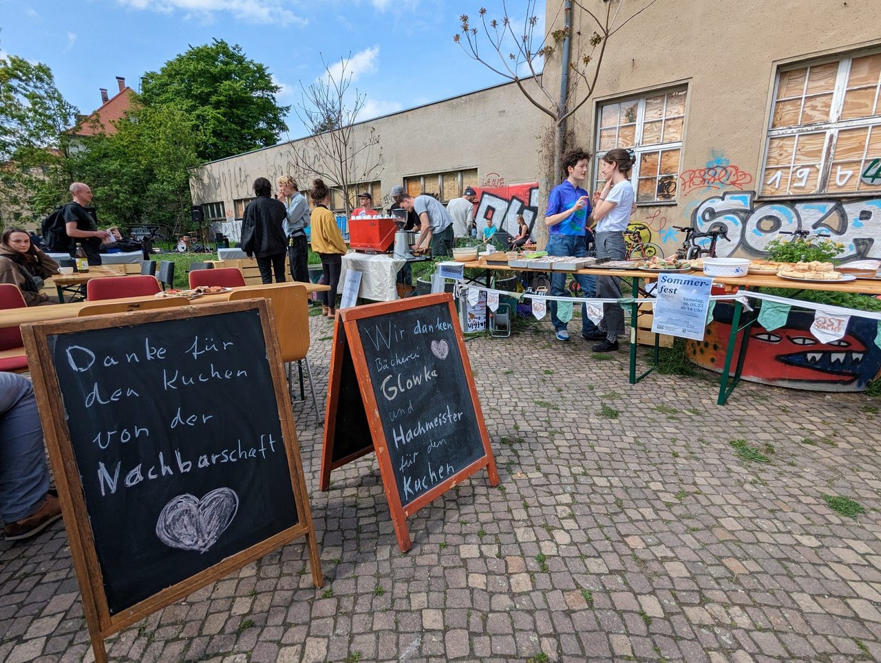 Blick auf zwei Schilder beim Nachbarschaftsfest. Auf dem linken Schild steht "Danke für den Kuchen von der Nachbarschaft" und auf dem rechten "Wir Danken Bücherei Glowka und Hachmeister für den Kuchen".