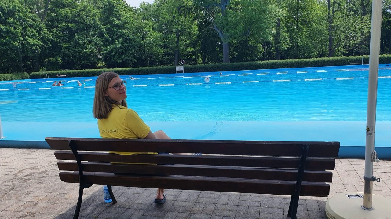  Paula Streit sitzt auf einer Bank an einem Schwimmbecken und schaut in die Kamera.