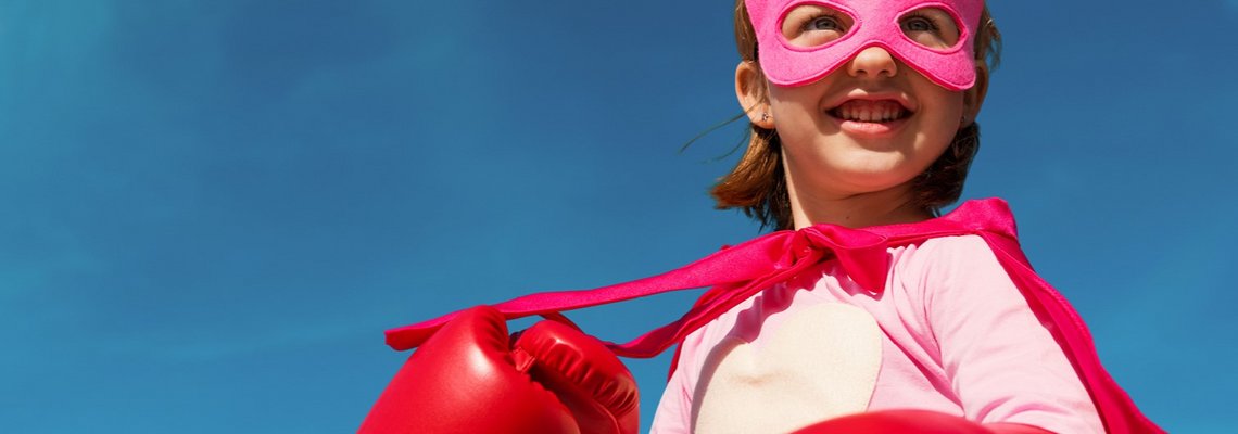 Ein Mädchen mit Superheldinnenbrille, Umhang und Boxhandschuhen.