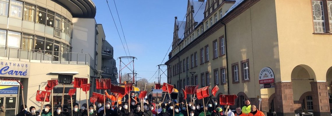 Eine große Gruppe Menschen stehen beieinander und halten rote Schneeschaufeln fest.