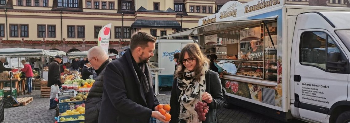 Zwei Personen schauen sich Obst an einem Stand auf dem Leipziger Markt an.