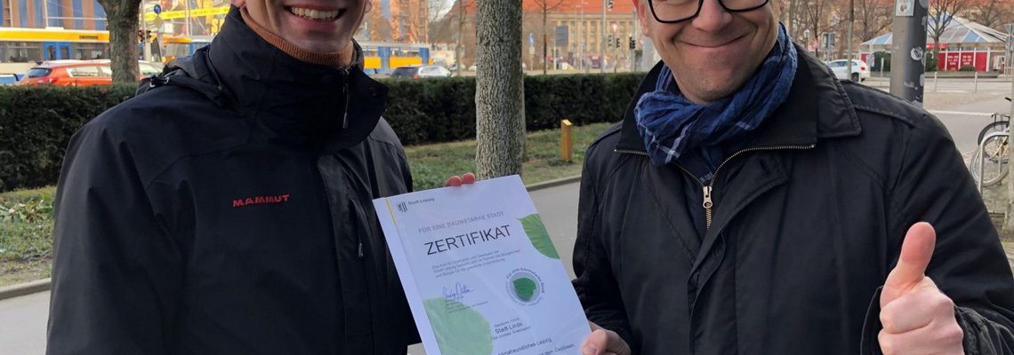  Nico Singer und Peter Krutsch lächeln in die Kamera und halten ein Zertifikat in den Händen.