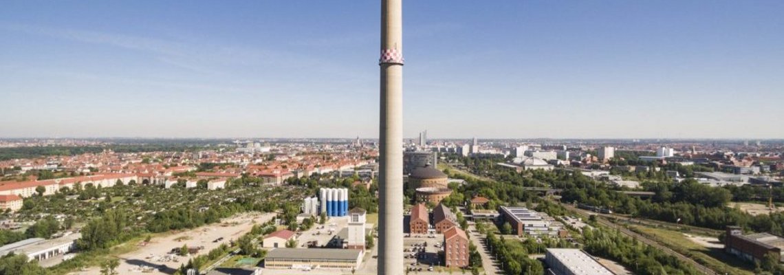 Der Schornstein ist von weitem zu sehen. Er steht in einer städtischen Umgebung.