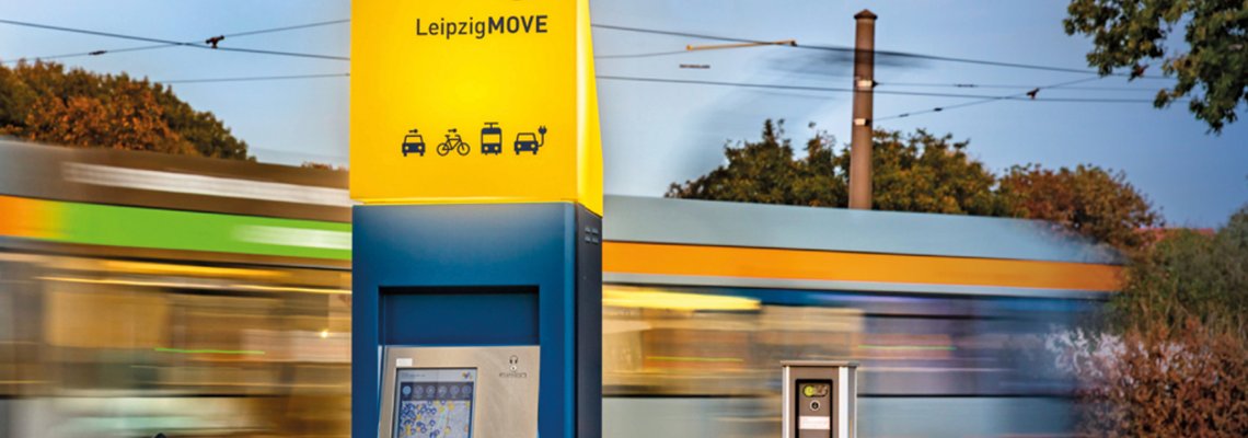 Hinter einer Mobilitätsstation fährt eine Straßenbahn entlang.