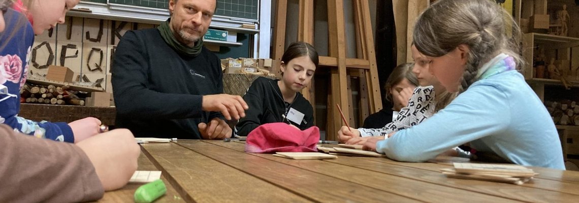 Erik Pomplitz sitzt mit mehreren Kindern an einem Tisch und unterhält sich mit ihnen.