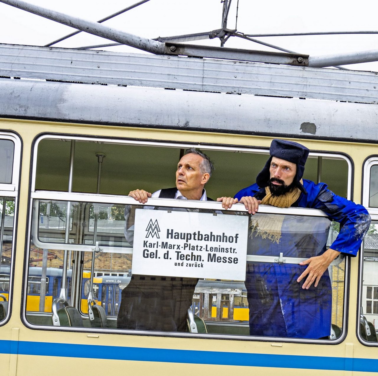 Zwei Männer schauen aus einer historischen Bahn heraus. Auf der Bahn ist ein Schild.