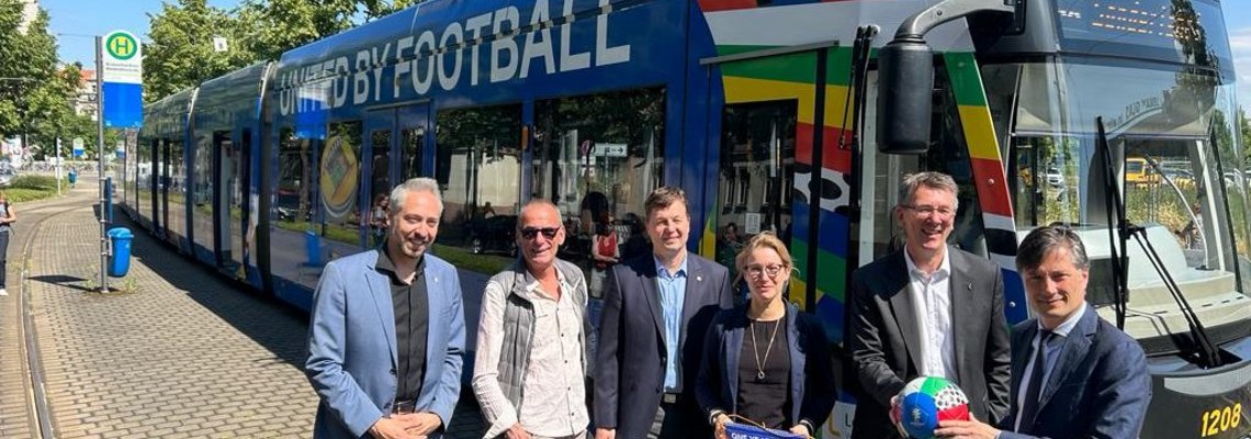 Einige Personen stehen vor einer Straßenbahn der LVB auf der"united by football" steht.