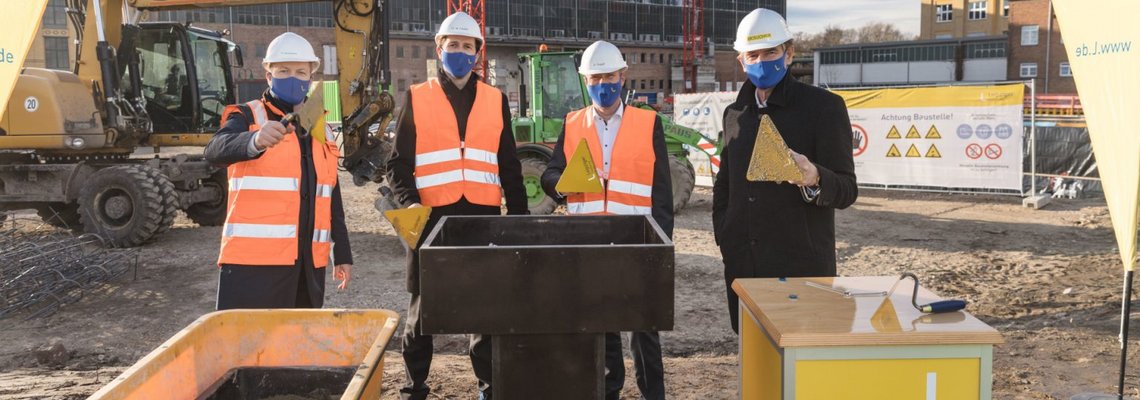 Thomas Brandenburg, Maik Piehler, Karsten Rogall und Burkhard Jung stehen auf der HKW Süd Baustelle und schauen in die Kamera. 