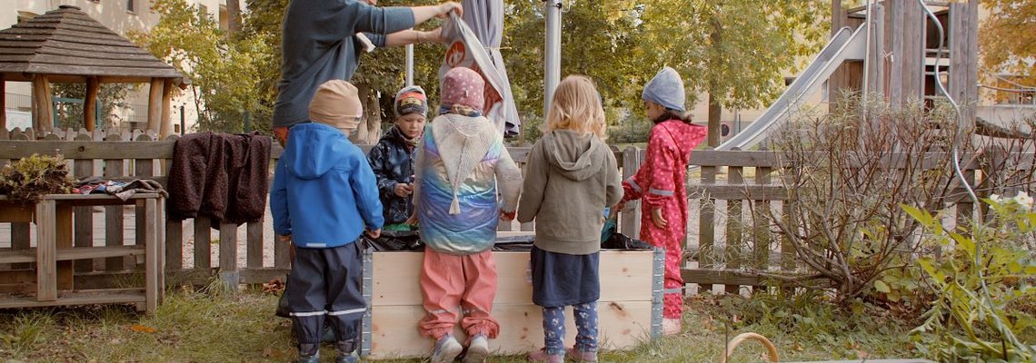 4 Kinder und ein Erwachsender spielen und arbeiten im Garten