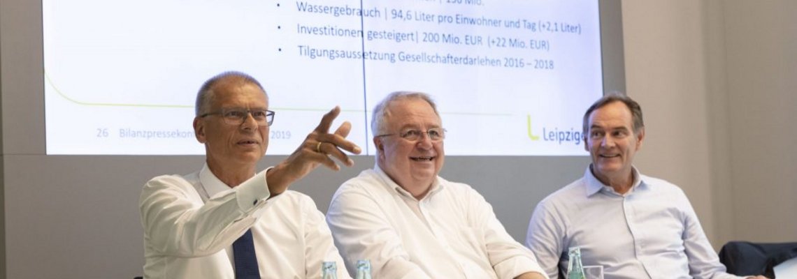 Auf dem Podium bei der Pressekonferenz reden drei Männer in hellen Hemden.