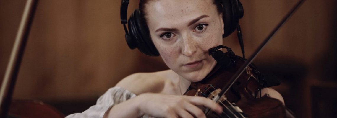 Eine Violinistin spielt konzentriert Geige und hat dabei Kopfhörer auf.