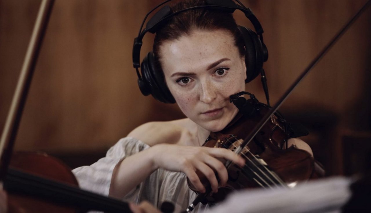 Eine Violinistin spielt konzentriert Geige und hat dabei Kopfhörer auf.