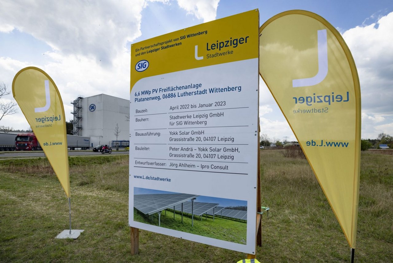 Ein Bauschild steht zwischen zwei Beach-Flags auf denen "Leipziger" steht.