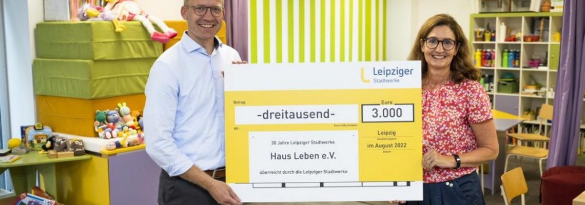 Zwei Personen halten einen sehr großen Scheck, auf dem "3000 Euro" steht.