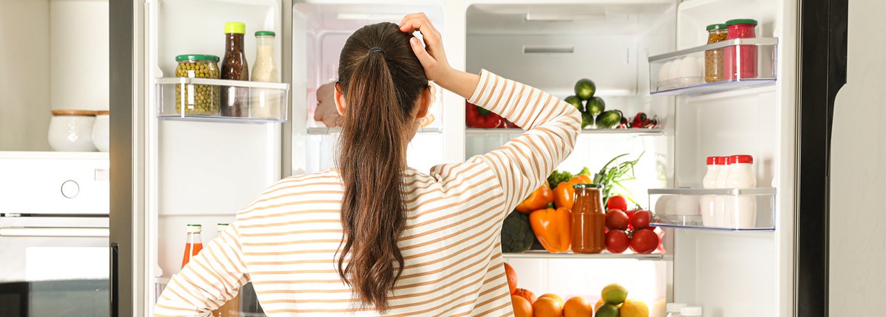 Eine Frau steht vor einem Kühlschrank, welcher mit Gemüse gefüllt ist