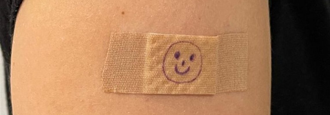 Ein Oberarm mit Pflaster, auf das ein Smiley gemalt worden ist.