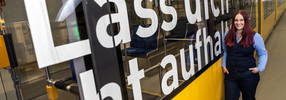 Eine Frau steht an eine Bahn gelehnt. Die Frau lächelt. Auf der Bahn steht "Lass dich nicht aufhalten"