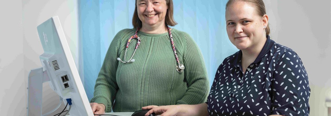 Martina Jacob und Dr. Katharina Reuse stehen an einem Tisch mit PC.