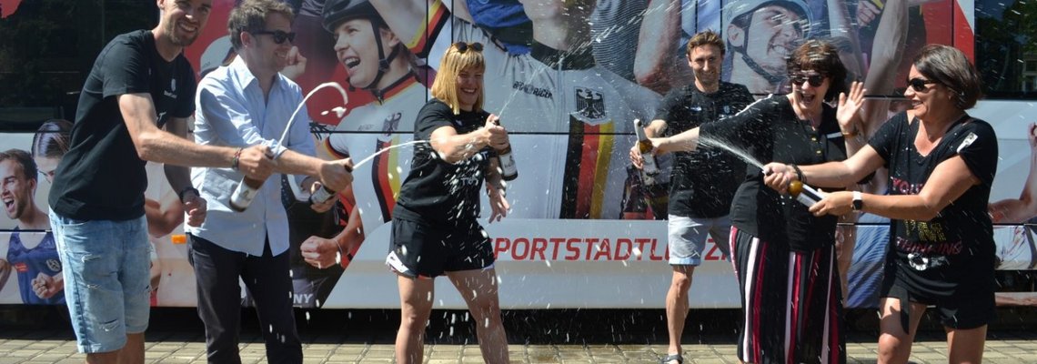 Mehrere Personen stehen vor der Leipziger Olympia-Bahn und weihen die Bahn mit alkoholfreiem Bier.