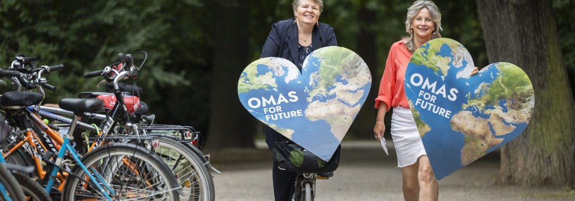 Zwei Frauen halten in einem Park zwei herzförmige Plakate in der Hand.