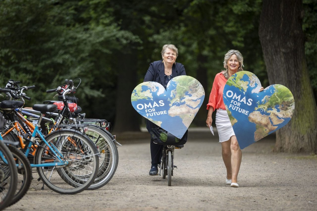 Zwei Frauen halten in einem Park zwei herzförmige Plakate in der Hand.