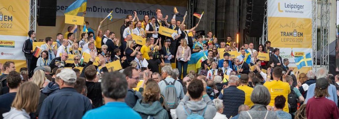 Eine Menschenmenge steht vor einer Bühne. Auf der Bühne wird ein Sieg gefeiert.