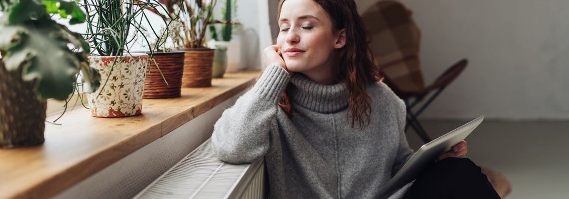Frau lehnt an Heizung und guckt aus dem Fenster