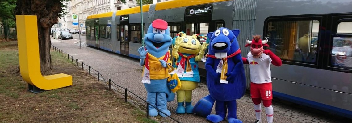 Vier Maskottchen stehen vor einer Straßenbahn.