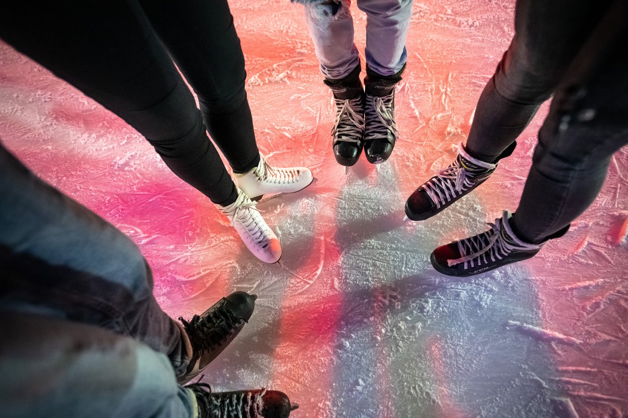 Mehrere Person stehen im Kreis auf einer Eisfläche. Das Bild zeigt das Eis und Schlittschuhe.
