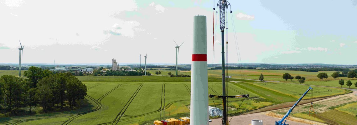 Sicht auf die Baustelle: Der Sockel des Windrads steht. Ein Kran steht daneben.