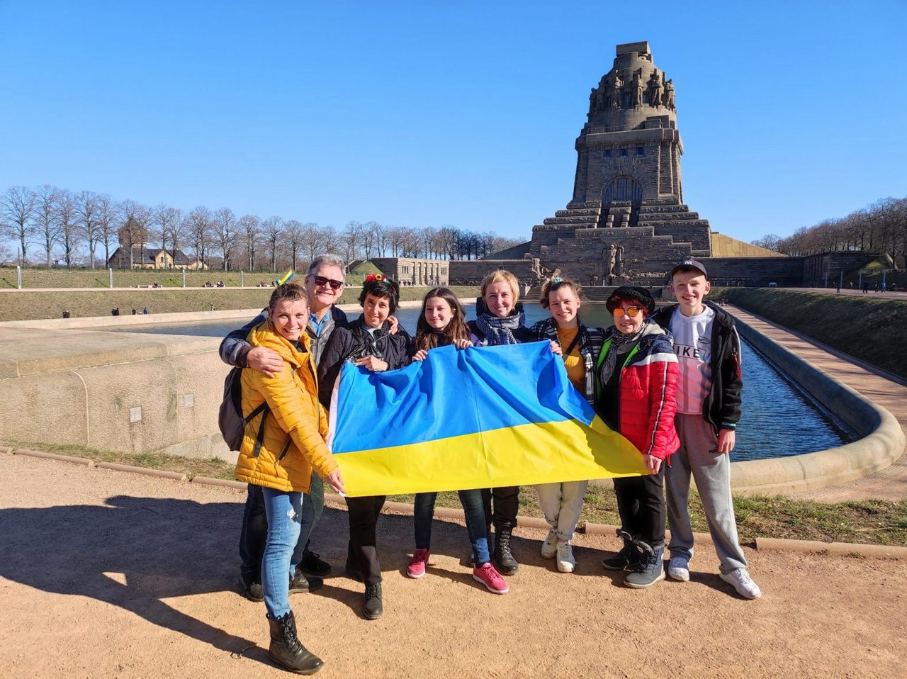 Sieben Personen stehen vor dem Völkerschlachtdenkmal und halten eine ukrainische Flagge.