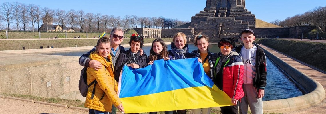 Sieben Personen stehen vor dem Völkerschlachtdenkmal und halten eine ukrainische Flagge.